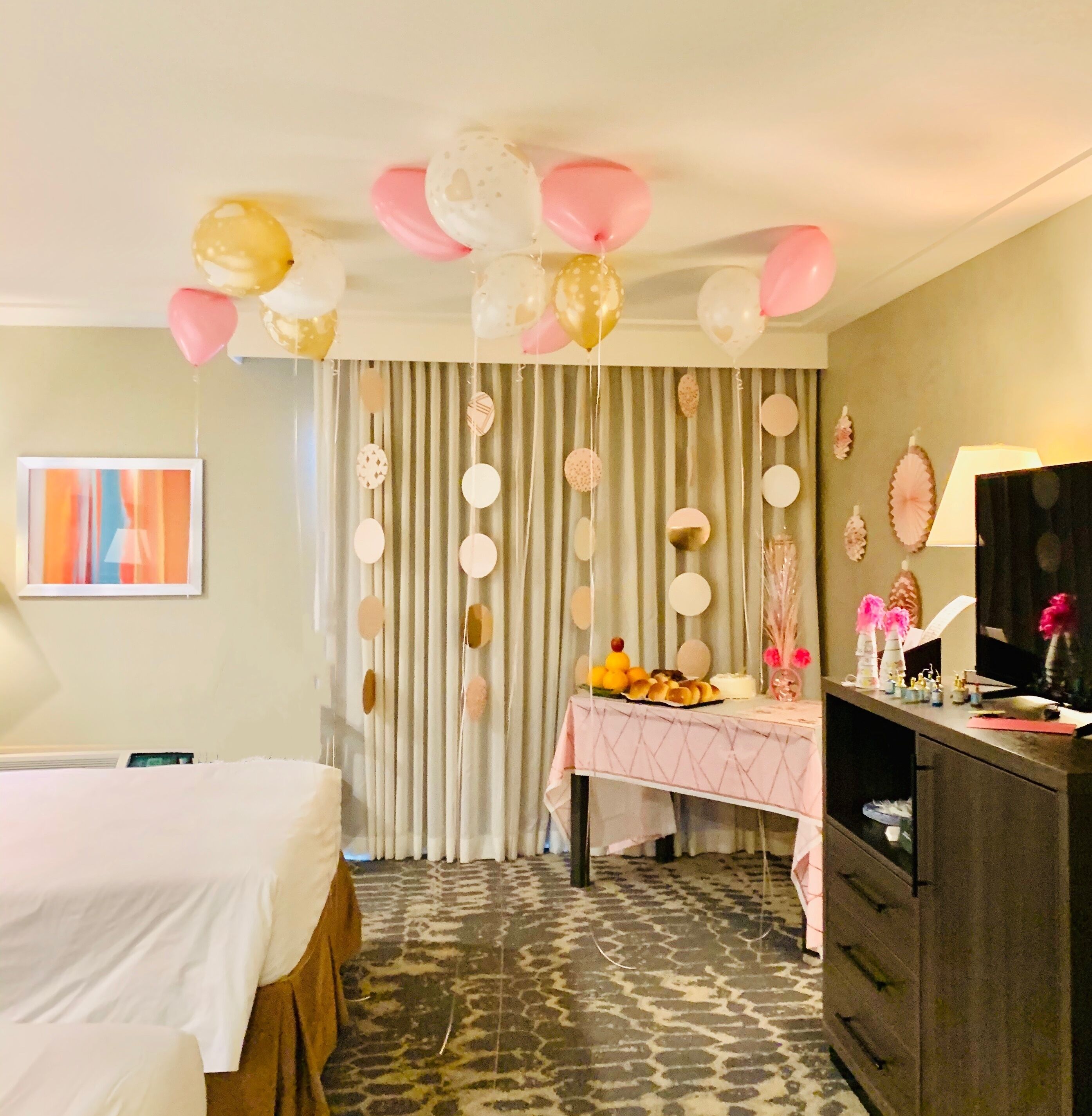A hotel room with a bed, a desk with a lamp, a dresser, and a curtain with hanging decorations.