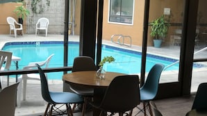 Ein Essbereich am Pool mit Blick auf ein Schwimmbecken, Sitzmöglichkeiten im Freien und einem Tisch mit einer Vase.