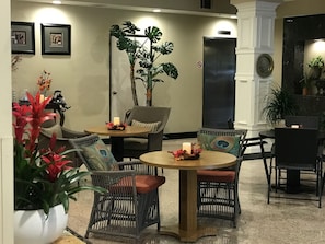 Un hall d’entrée avec des meubles en osier, une grande plante en pot et des tableaux encadrés accrochés au mur.