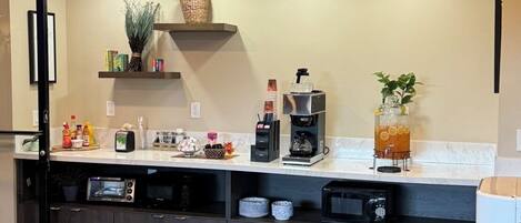 A modern kitchen with dark cabinetry, a built-in microwave, a coffee maker, and a shelf with decorative items.