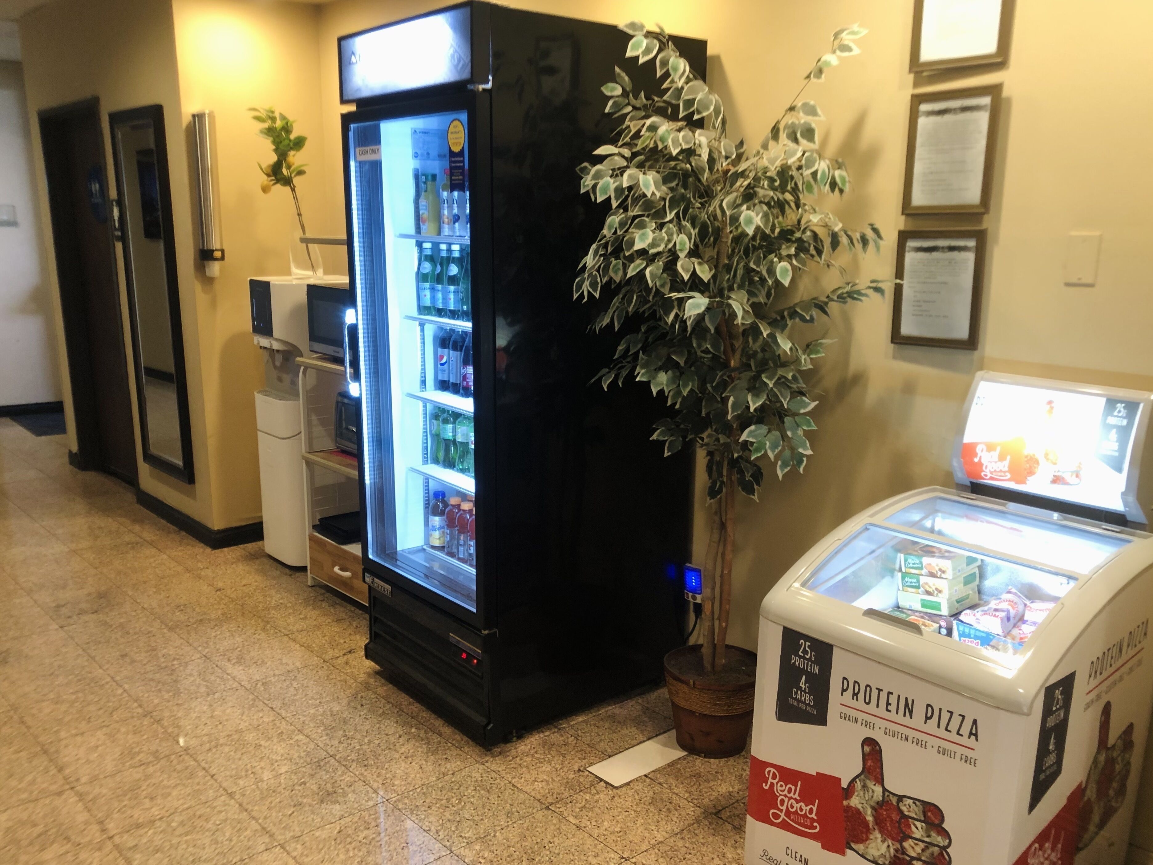 Un hall d’hôtel équipé d’un distributeur automatique de boissons en libre-service, d’un présentoir réfrigéré et d’un distributeur automatique de pizzas riches en protéines.
