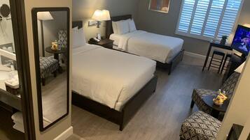 A hotel room with two beds, a desk, a chair, a TV, and a window with blinds.