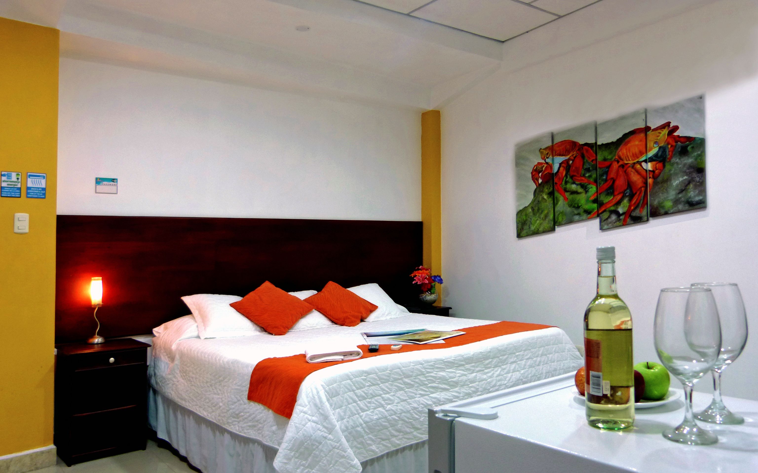 A hotel room with a bed, a nightstand, a painting, a bottle, and glasses.