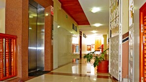 A hotel corridor with elevators, a potted plant, and a red-framed door. - Hotel Brisas Del Pacifico (Puerto Ayora)