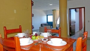 A dining area with a wooden table set for two, including plates, bowls, cutlery, and a fruit bowl. - Hotel Brisas Del Pacifico (Puerto Ayora)