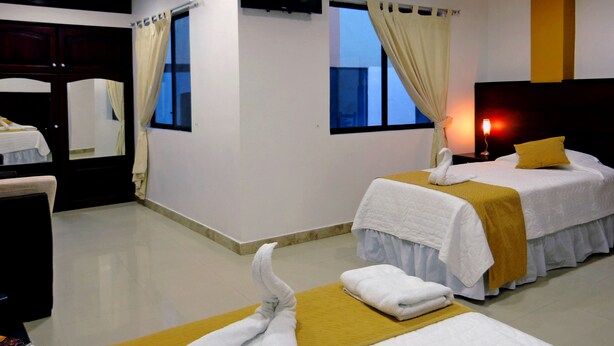 A hotel room with two beds, a TV, a window with curtains, and a nightstand with a lamp. - Hotel Brisas Del Pacifico (Puerto Ayora)