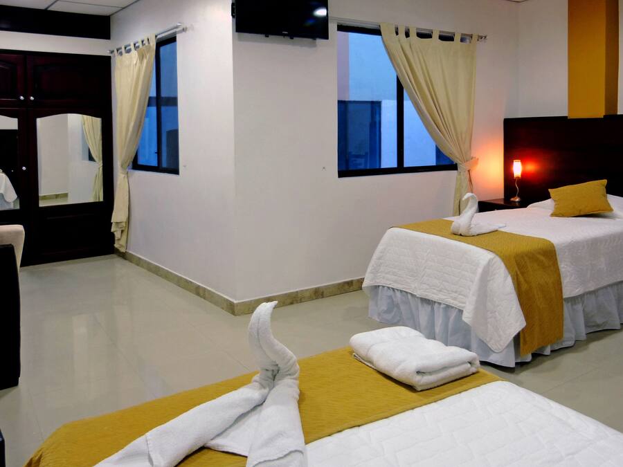 Quarto de hotel com duas camas, televisão, janela com cortinas e mesa de cabeceira com abajur.