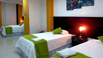 Quarto de hotel com duas camas, cada uma com roupa de cama branca e detalhes verdes, uma mesa de cabeceira com abajur e um quadro na parede.