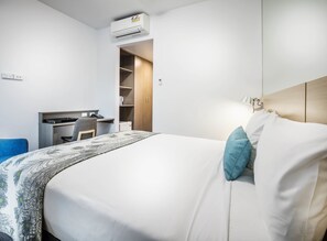 A hotel room with a bed, a desk, a chair, a wardrobe, and an air conditioning unit.