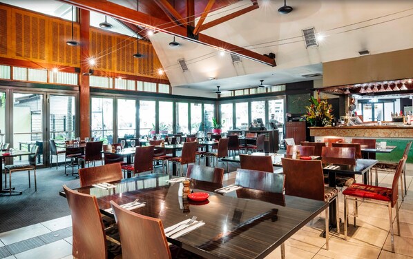 Ein geräumiges Restaurant mit hohen Decken, großen Fenstern und unterschiedlichen Sitzmöglichkeiten, darunter Tische und Stühle.