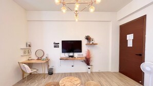 A modern room with a wooden floor, a round table with four stools, a television on a wooden stand, a small desk with a chair, and a door with a sign. - Three Brothers B&B (Taitung)