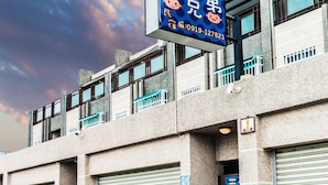 A building with a blue sign, closed garage doors, and potted plants on the sidewalk. - Three Brothers B&B (Taitung)