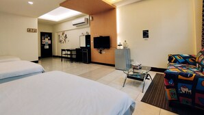 A hotel room with two beds, a desk with a chair, a television, an air conditioning unit, and a colorful sofa. - Huadong Homestay (Taitung)