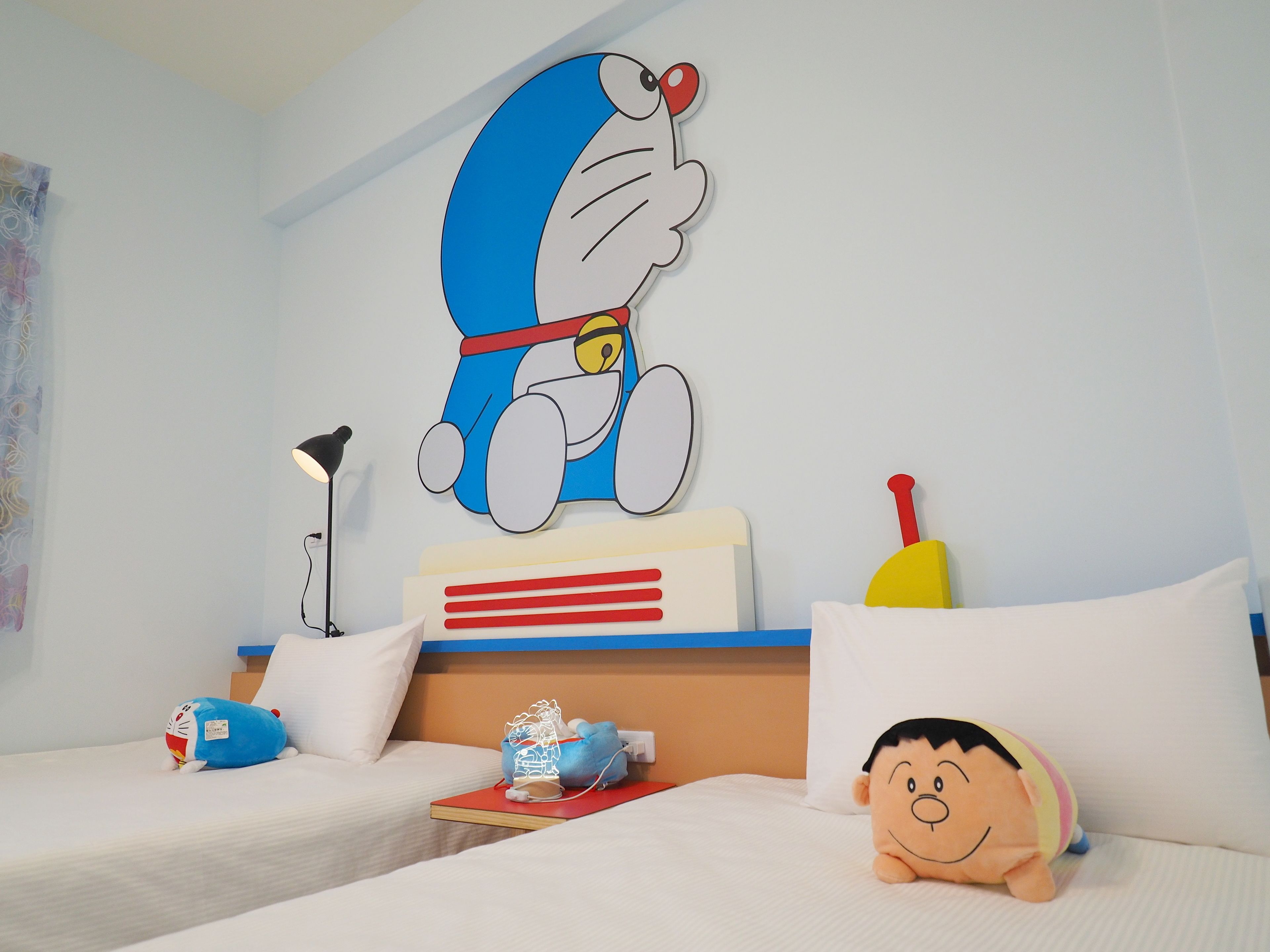 A hotel room with two beds, a large wall mural of a cartoon character, a lamp, a stuffed toy, and a pillow.