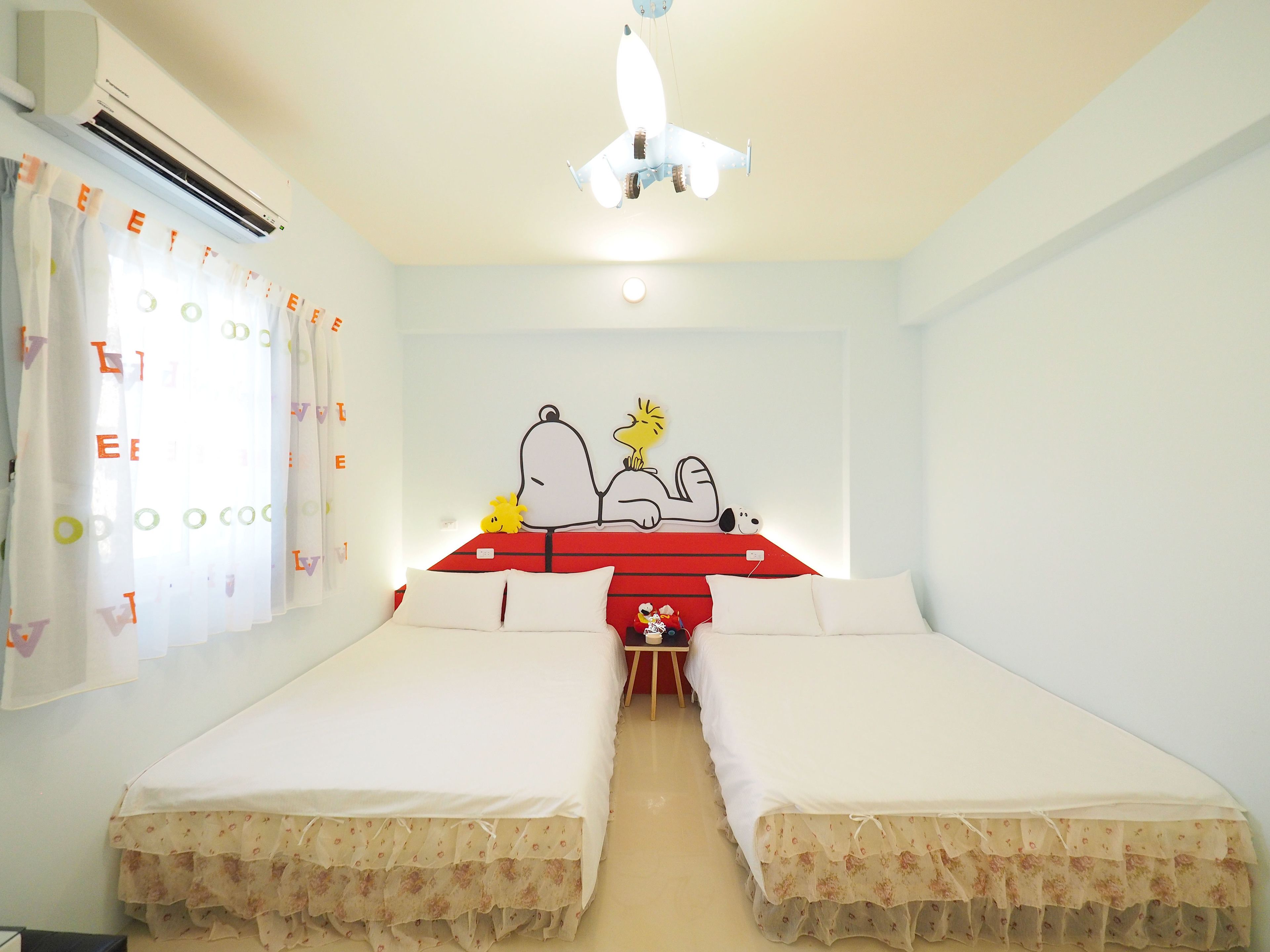 A room with two beds, a ceiling fan, and a wall decoration of Snoopy and Woodstock.