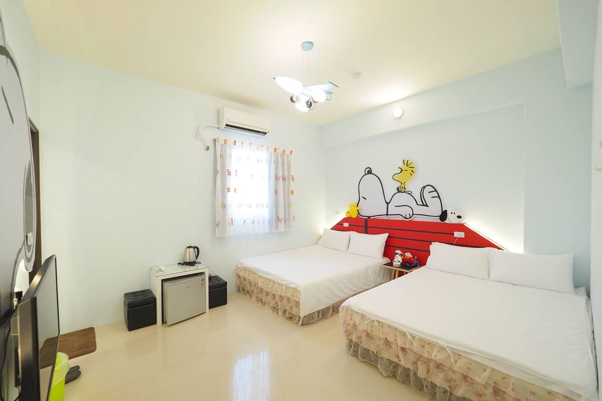 Habitación de hotel con dos camas, un ventilador de techo, un equipo de aire acondicionado, una mesita con un hervidor y un adorno en la pared.