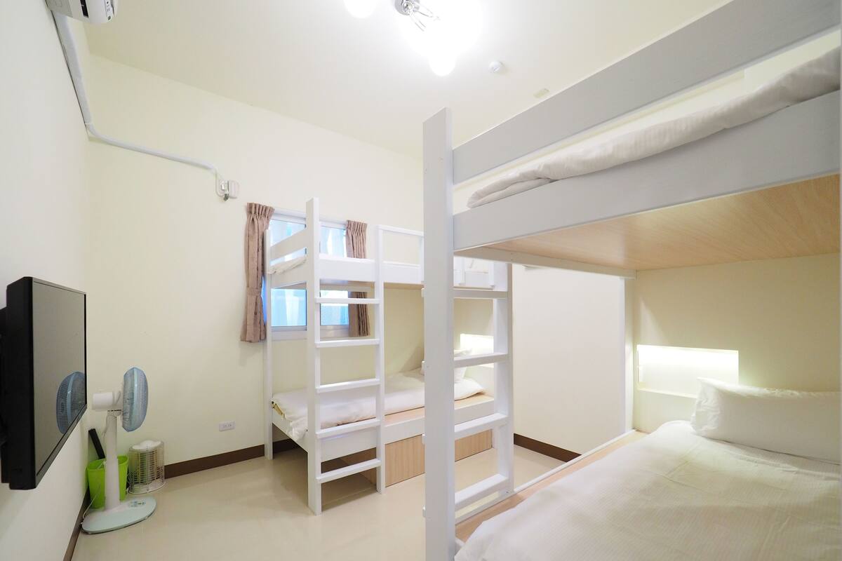 Habitación con literas, televisor, ventilador y ventana con cortinas.