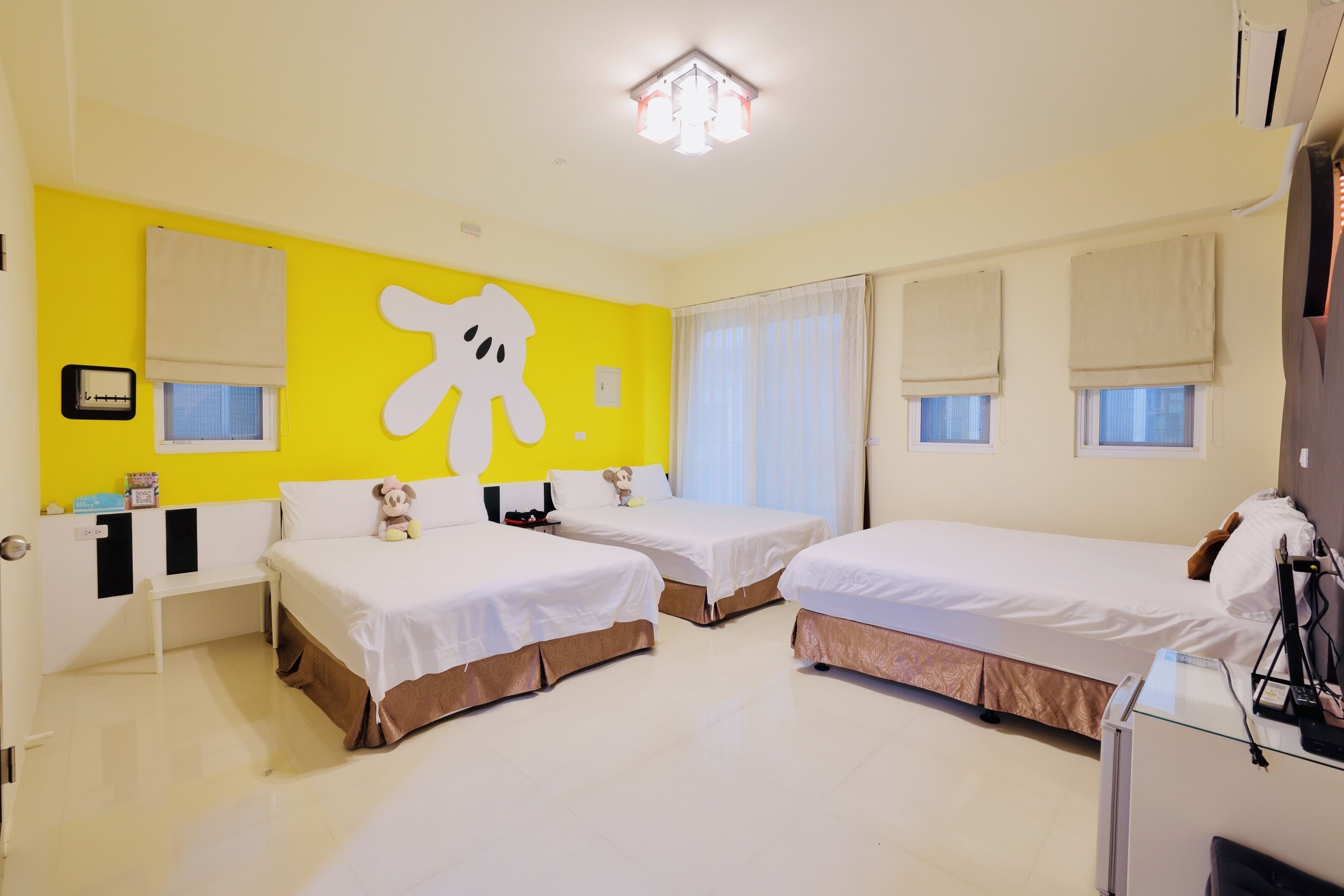 Una habitación de hotel con dos camas, un gran oso de peluche decorando la pared y un pequeño escritorio con una lámpara.