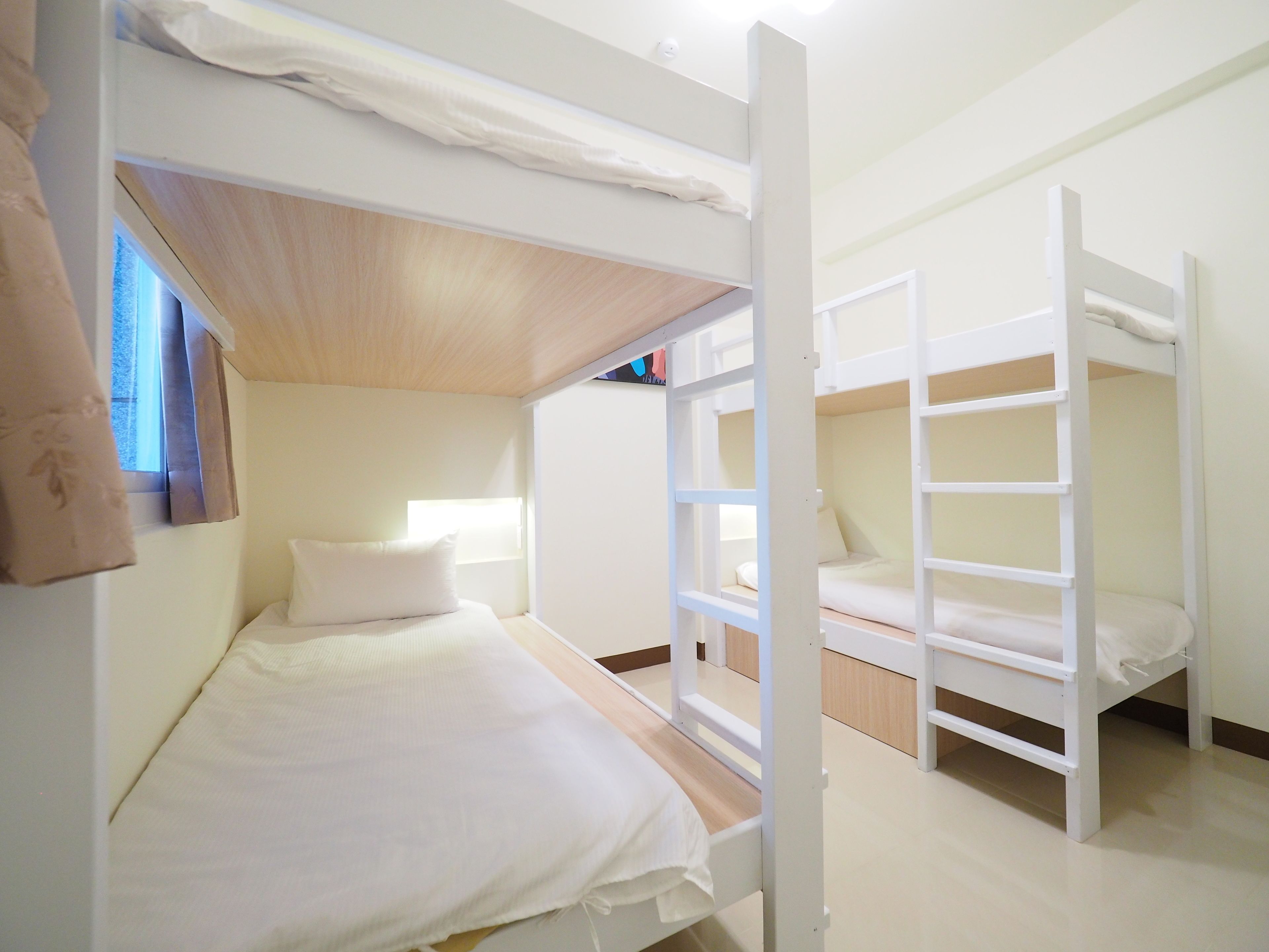 A bunk bed room with a wooden ceiling, white bedding, and a window with curtains.