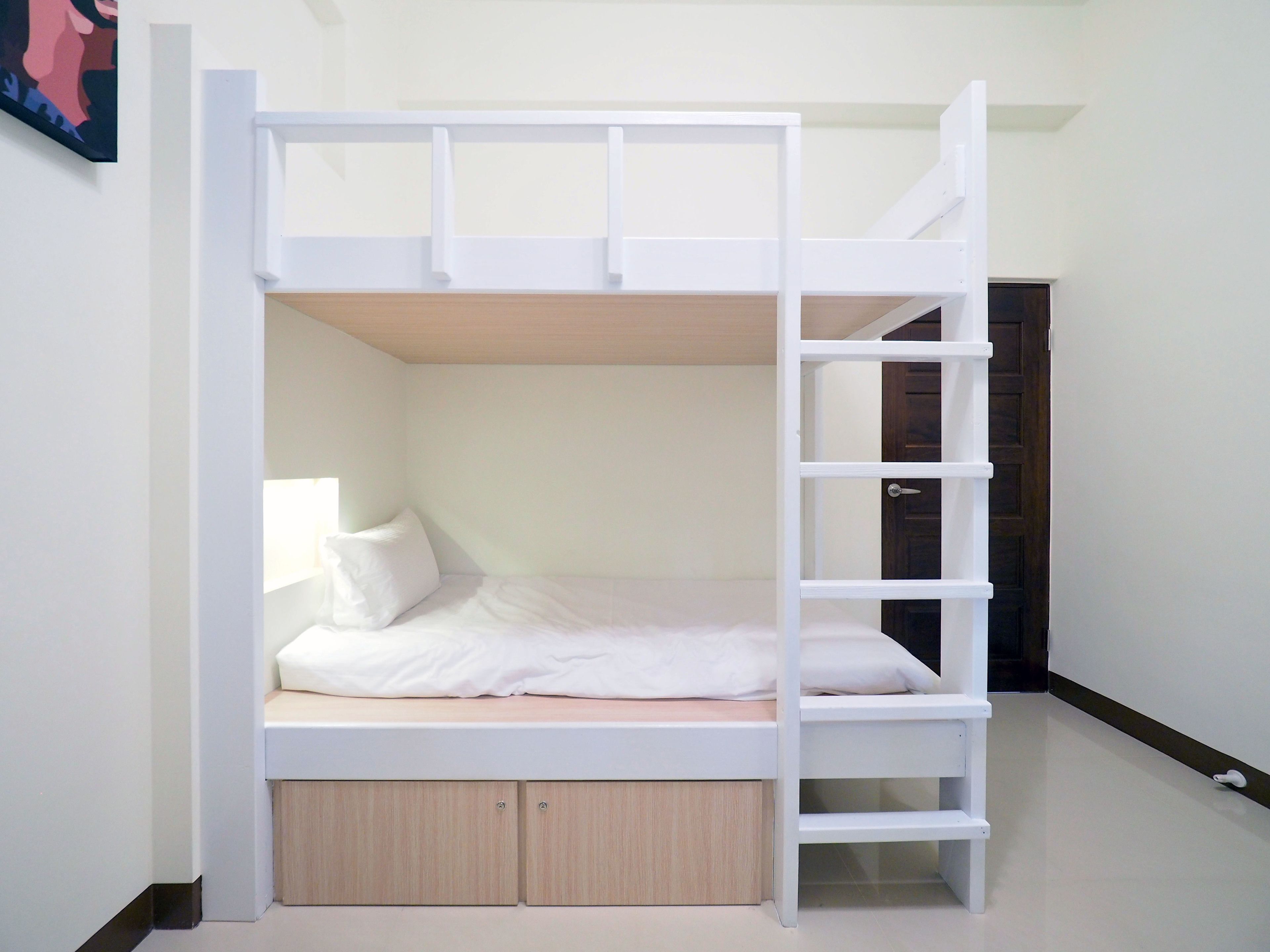 Una cama litera con una escalera, una mesita de noche y una puerta al fondo.