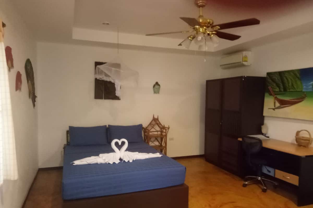 Quarto com cama, escrivaninha, cadeira, ventoinha no teto e um quadro na parede.