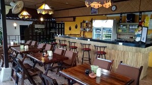 A restaurant with wooden tables and chairs, a bar area, and a refrigerator stocked with beverages. - Bee Nat Garden Resort (Koh Samui)
