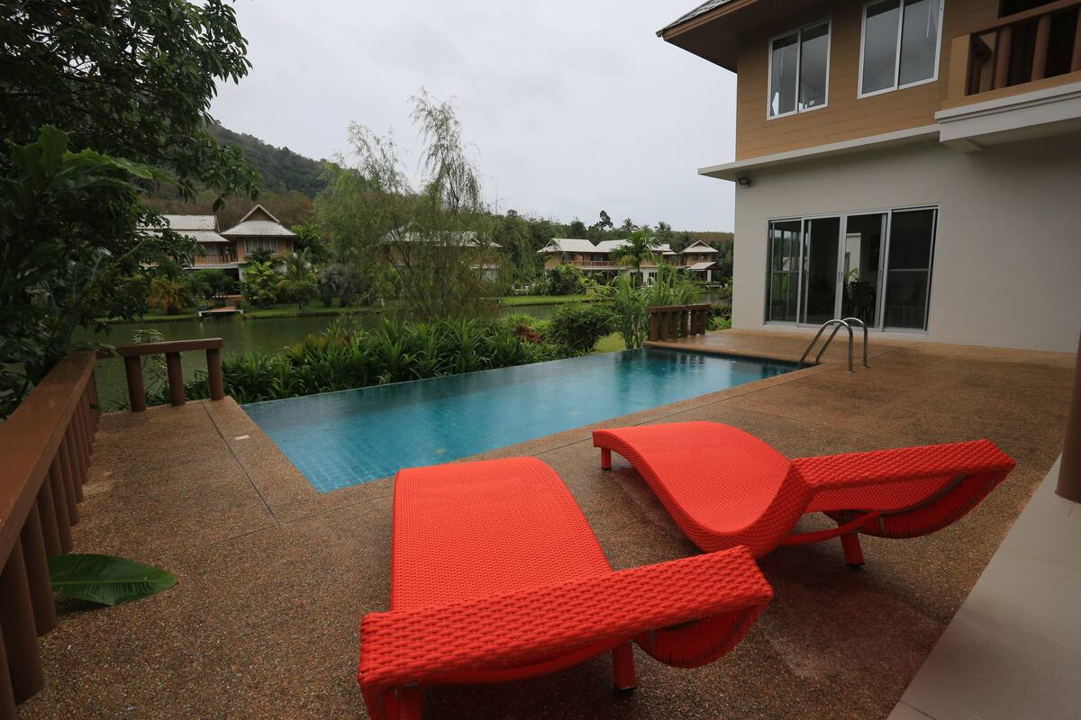 A swimming pool with two red lounge chairs, surrounded by greenery and a view of a hillside.