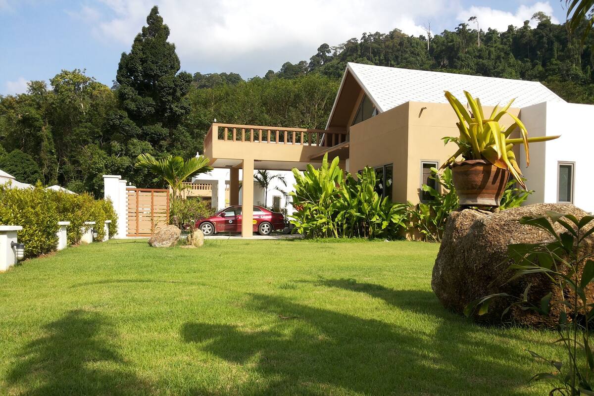 A modern house with a car parked in front, surrounded by lush greenery and a well-maintained lawn.