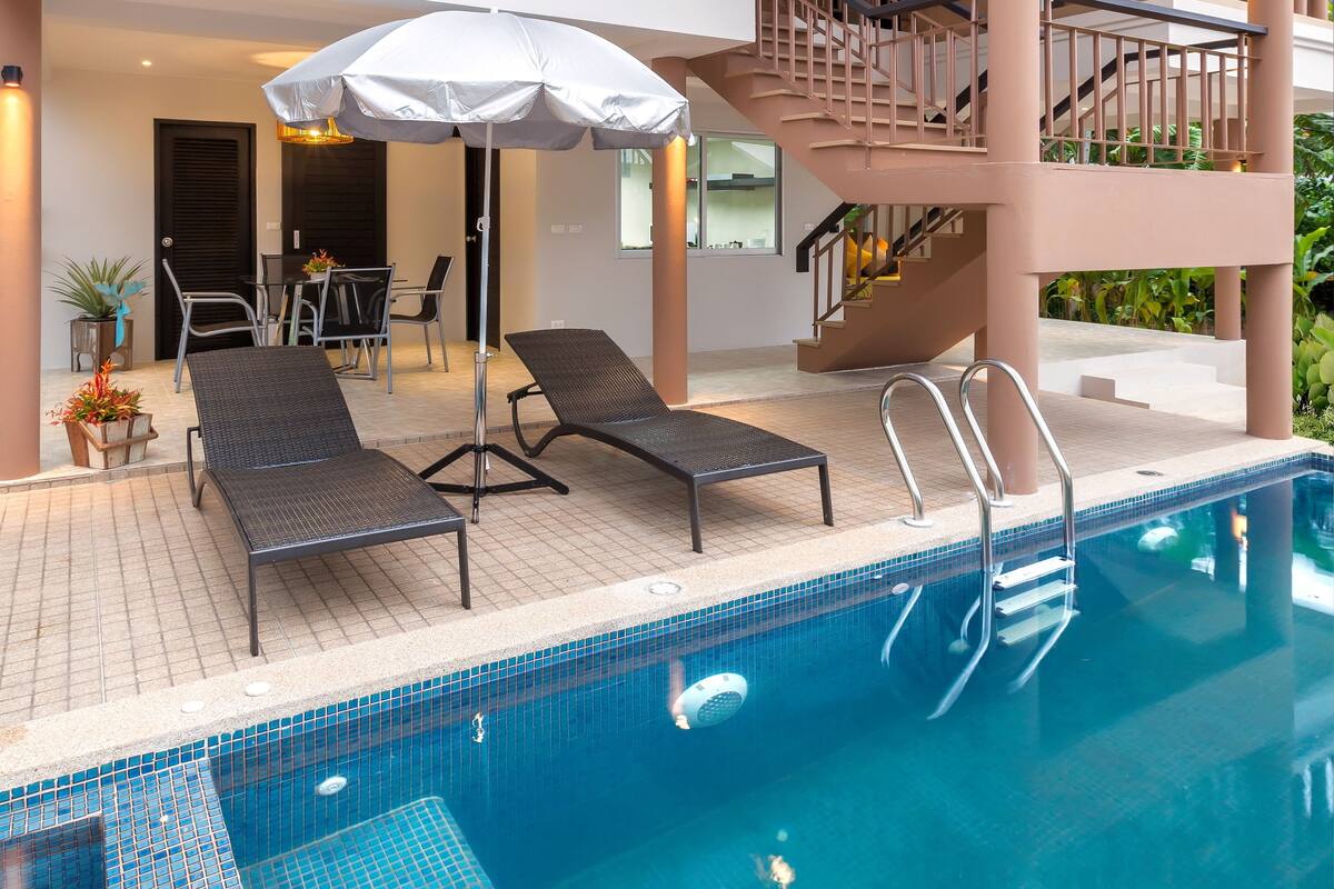 A modern hotel with a swimming pool, lounge chairs, and a staircase to the upper floor.