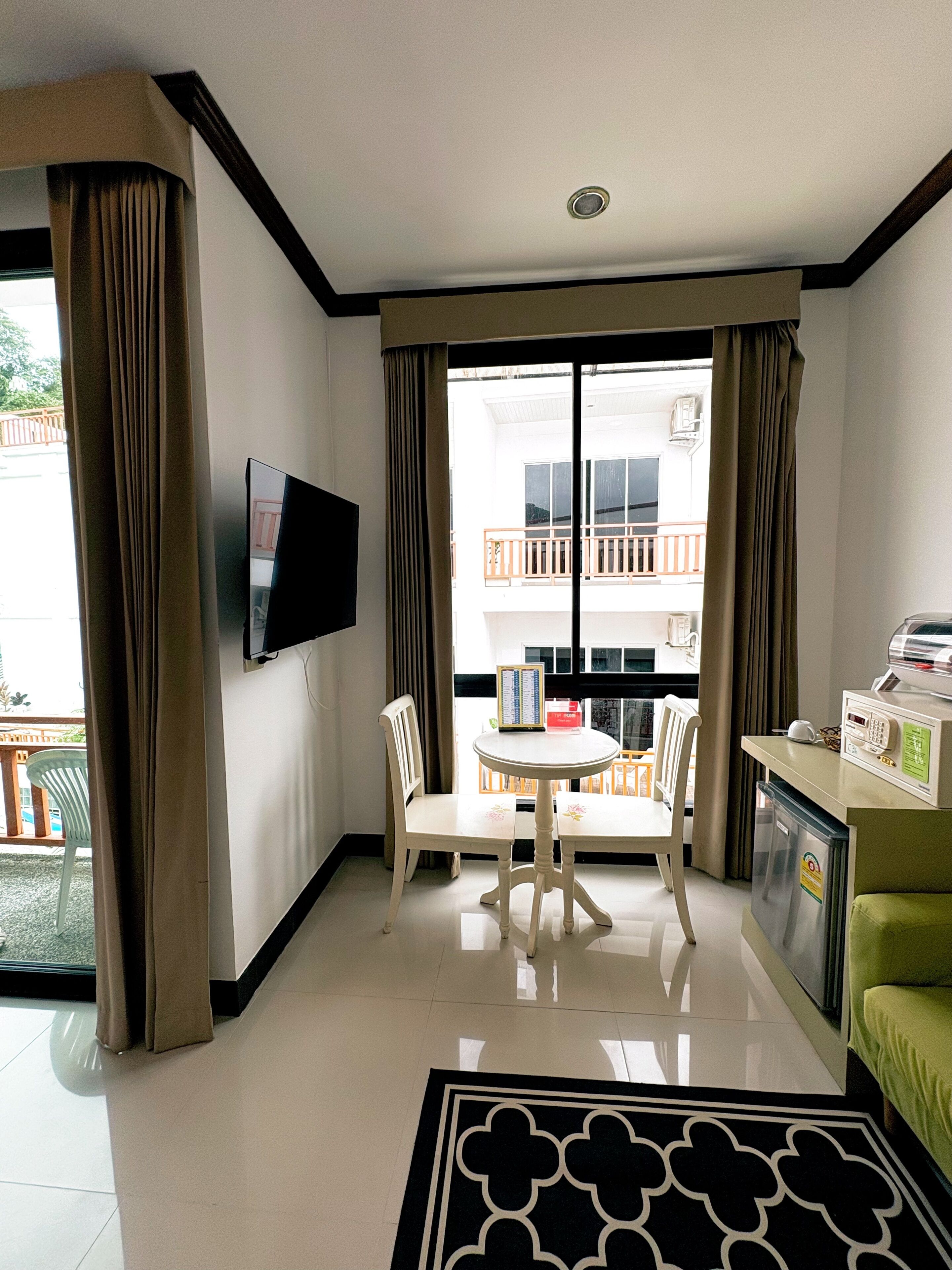 Habitació d'hotel amb televisió de pantalla plana penjada a la paret, taula de menjador amb cadires, nevera petita i un sofà verd.