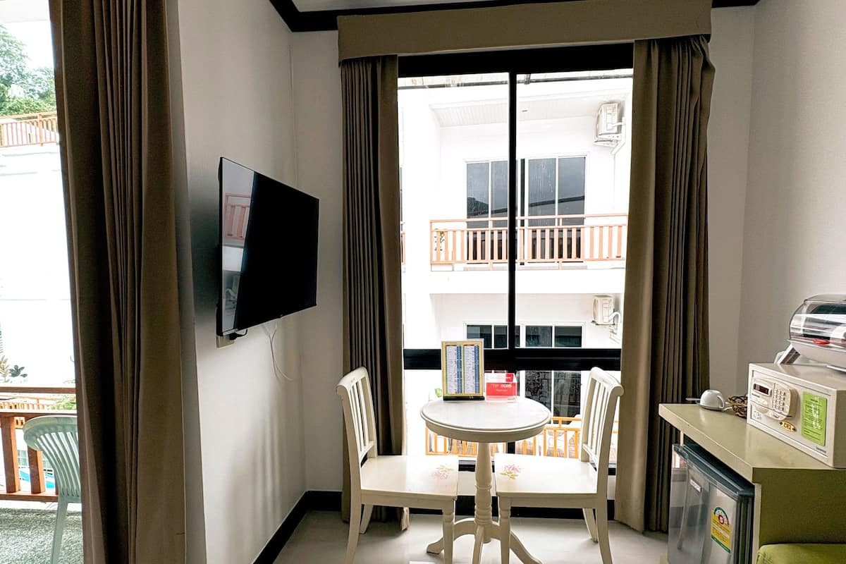Une chambre d’hôtel équipée d’un téléviseur à écran plat fixé au mur, d’une table à manger avec des chaises, d’un petit réfrigérateur et d’un canapé vert.