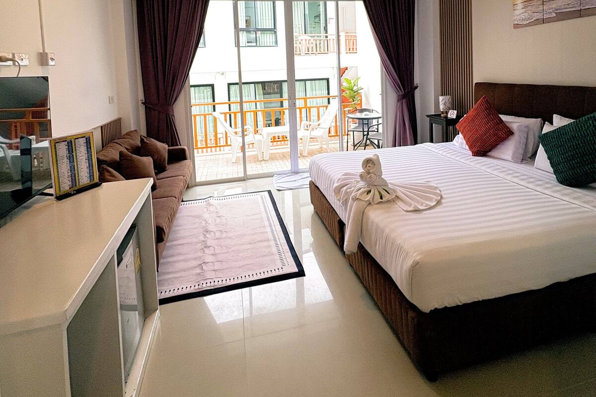 Une chambre d’hôtel comprenant un lit, un bureau, une chaise, un canapé, un balcon avec des chaises et un ventilateur de plafond.
