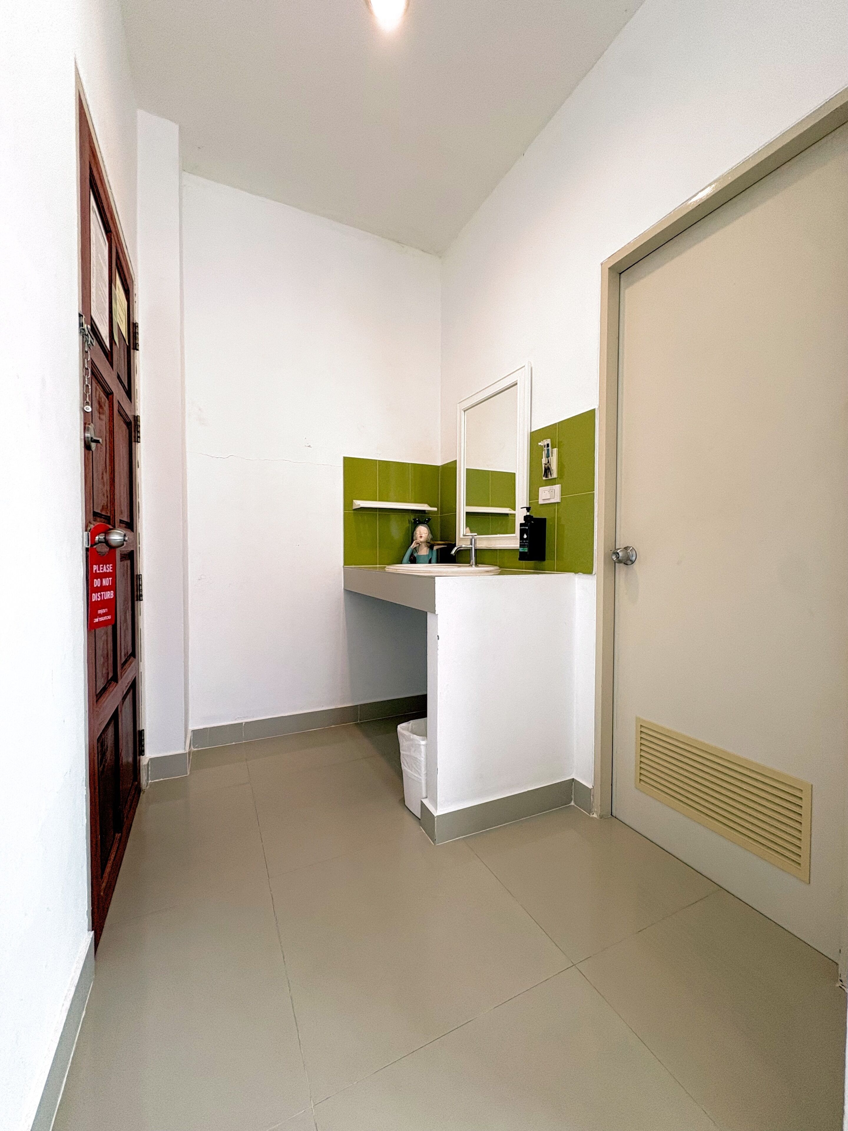 A bathroom with a white sink, green-tiled walls, a mirror, and a door.