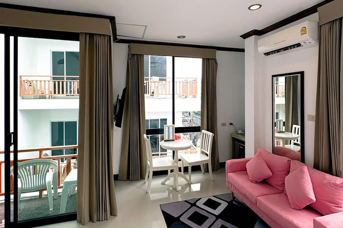 Un salon moderne avec un canapé rose, une table à manger avec des chaises, un balcon doté d’une balustrade et une grande fenêtre.