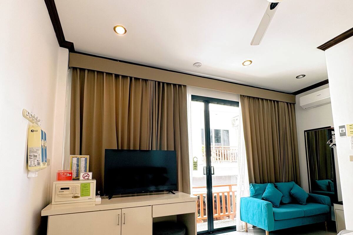Une chambre d’hôtel avec un lit, un téléviseur posé sur un bureau, un ventilateur de plafond et une vue sur l’extérieur.