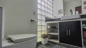 Un baño con inodoro, lavabo, espejo y ventana con vidrio esmerilado.