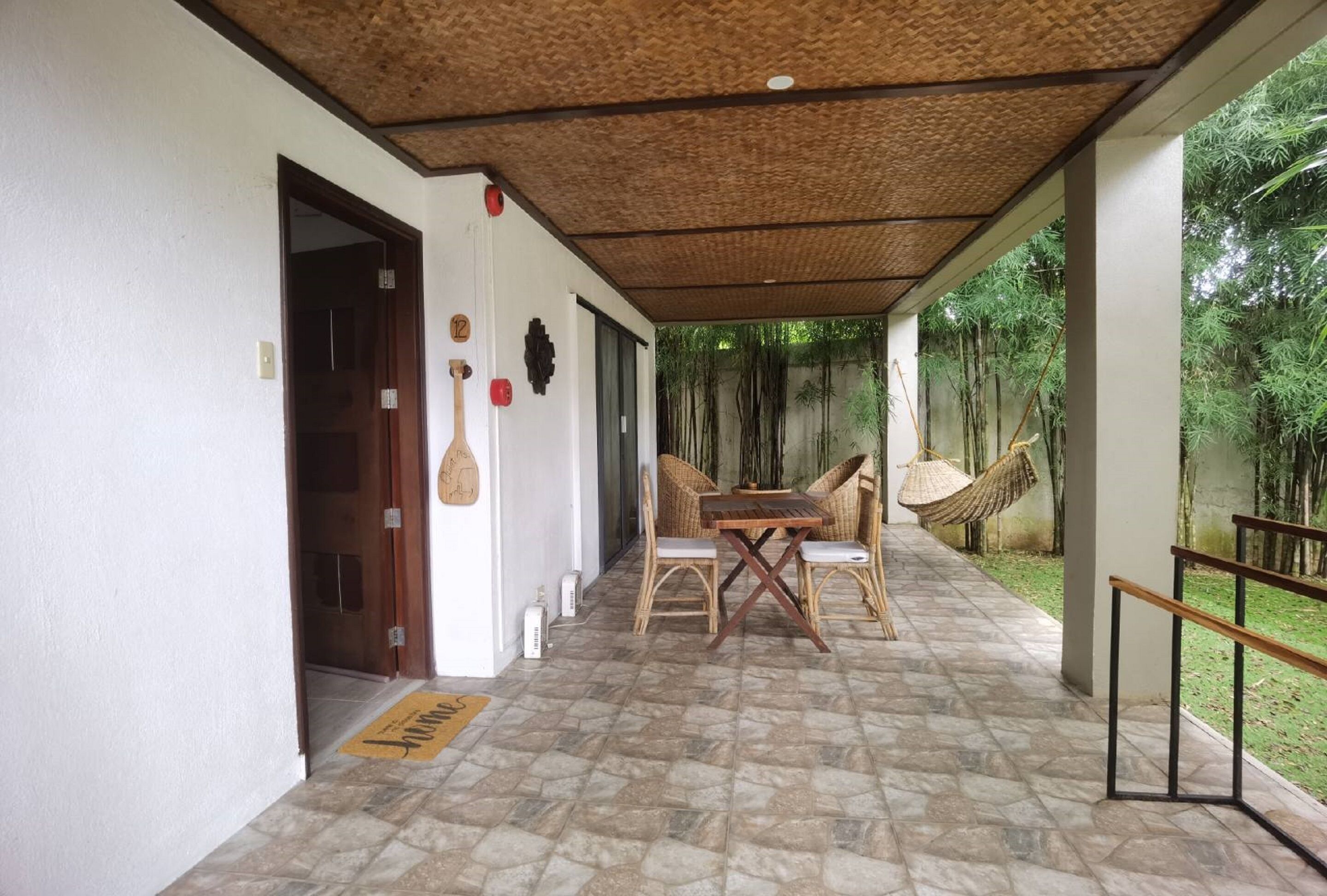 Un espacio al aire libre techado con suelo de piedra, una mesa y sillas de madera, y una hamaca.