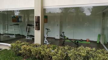 A modern gym with exercise equipment, including treadmills and stationary bikes, and a glass wall reflecting the surroundings.