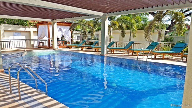 Una piscina con sillas de descanso, una pérgola y un área cubierta con toldo blanco.
