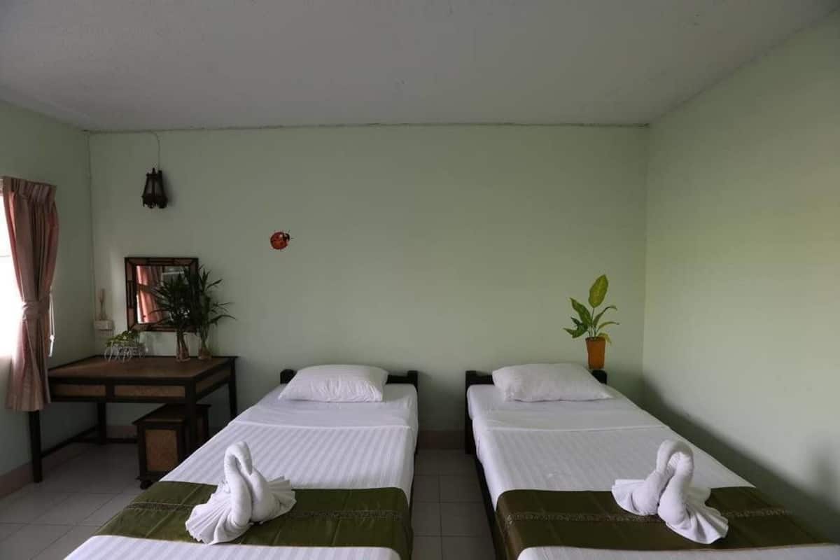 Una habitación con dos camas, un escritorio, una silla, una planta en maceta y un reloj de pared.