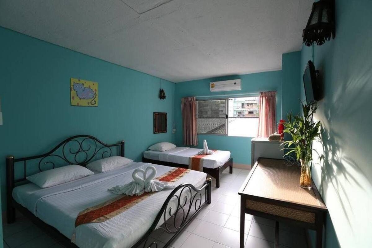Una habitación con dos camas, una mesita, una ventana con cortinas y un aire acondicionado de pared.