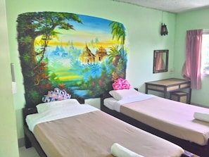 A room with two single beds, a small table, a wall tapestry, and a window with curtains.