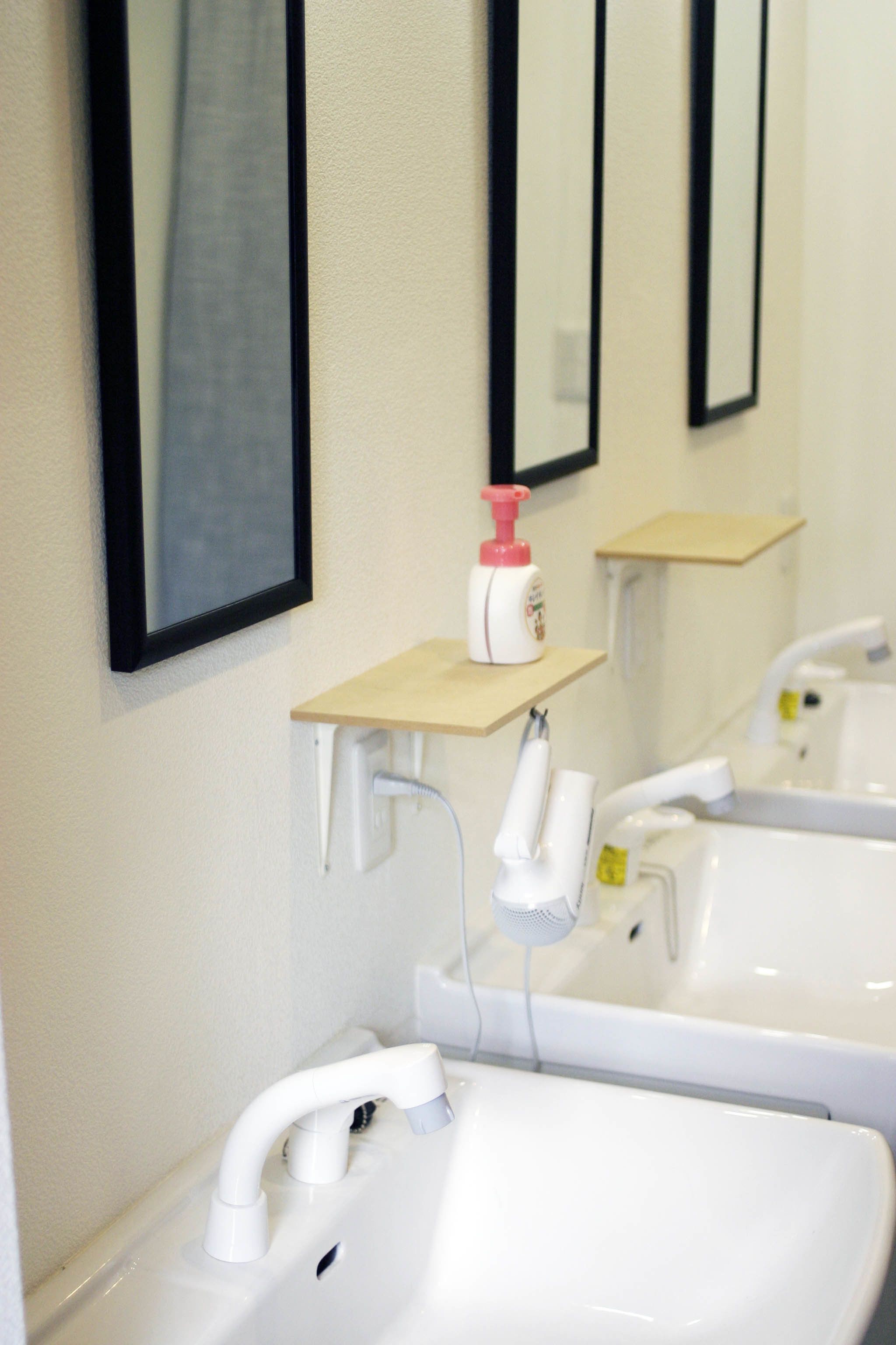 A bathroom with two sinks, a mirror, and a soap dispenser on a shelf.