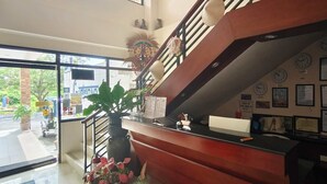 Un espace d’accueil comprenant un escalier, une plante en pot et un mur orné d’horloges et de certificats.