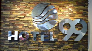 Señal de hotel con el nombre "HOTEL 99" sobre una pared de ladrillo texturizado.