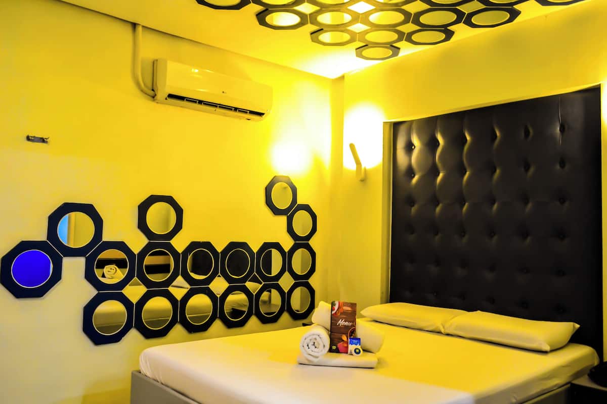 A hotel room with a bed, a wall-mounted air conditioner, and a decorative wall with circular mirrors.