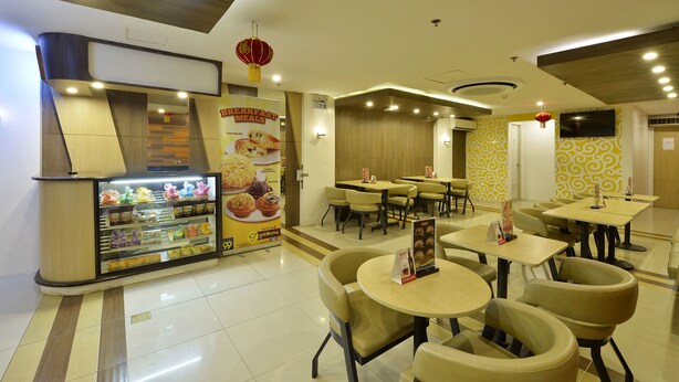 Un restaurante moderno con un mostrador que exhibe alimentos, varias mesas y sillas, y una pantalla de televisión en la pared.