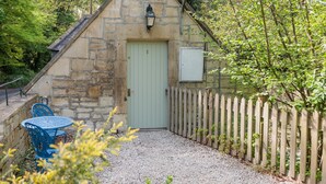 A stone building with a green door, a wooden fence, and a gravel path. - The Coach House (Corsham)