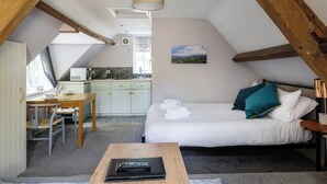 A compact room with a bed, a small desk, and a kitchenette. - The Coach House (Corsham)