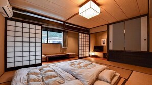 A traditional Japanese-style room with tatami flooring, a futon bed, sliding shoji doors, and a television. - BENIKEA Yufuin Kinrinko Hotel Museum (Yufuin)